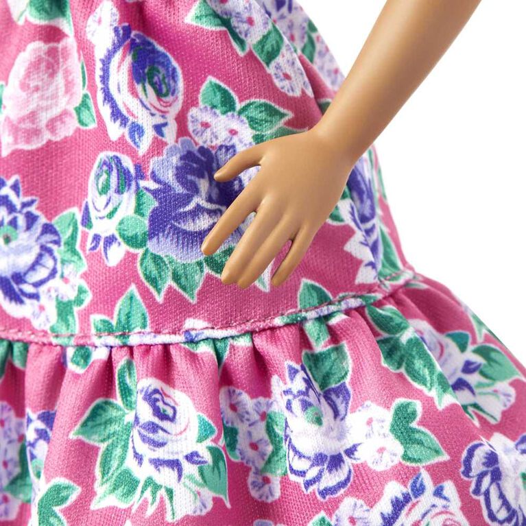 Poupée ​Barbie Fashionistas 150 chauve, vêtue d'une robe rose florale, de bottillons blancs et de boucles d'oreilles
