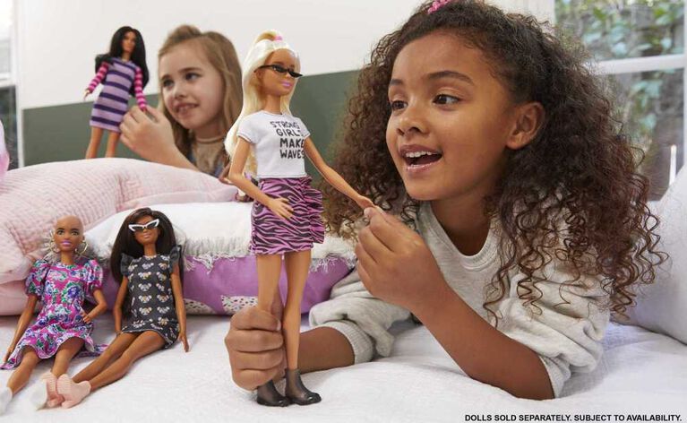 Poupée ​Barbie Fashionistas 150 chauve, vêtue d'une robe rose florale, de bottillons blancs et de boucles d'oreilles